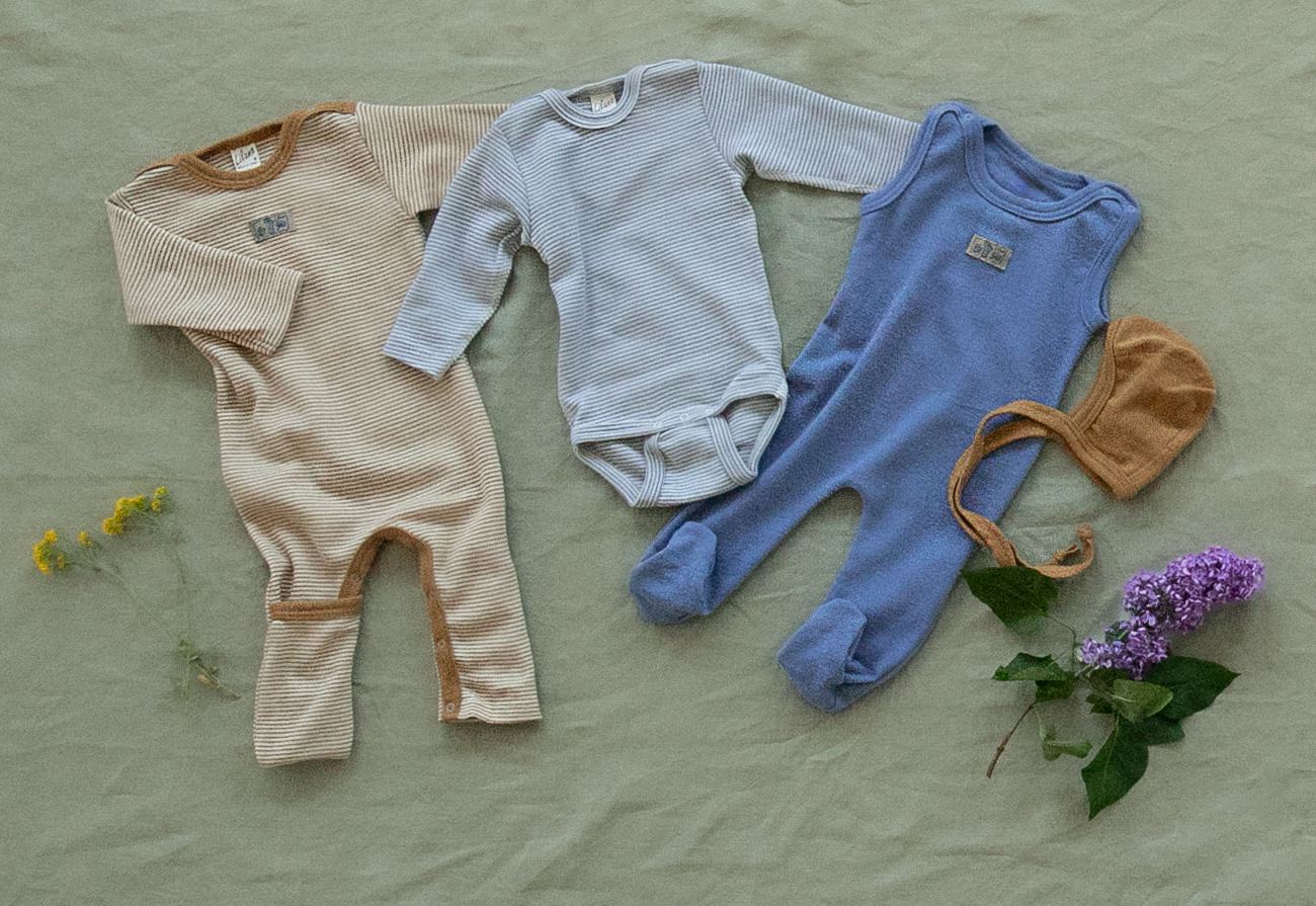 Babykleidung aus Wolle Seide von Lilano liegt auf einer grünen Decke.