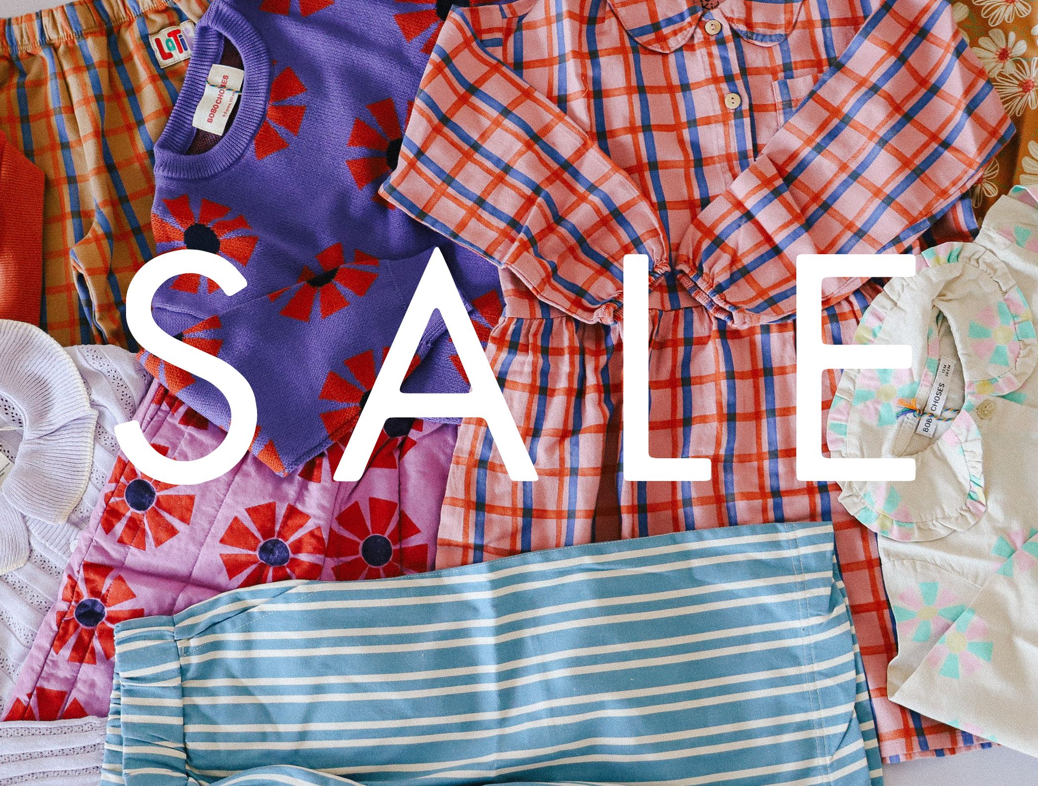 Diverse preisreduzierte Kinderkleidung und Babykleidung aus Baumwolle Wolle Seide von Lilano in roten und blauen Farben liegen auf einem Dielenboden