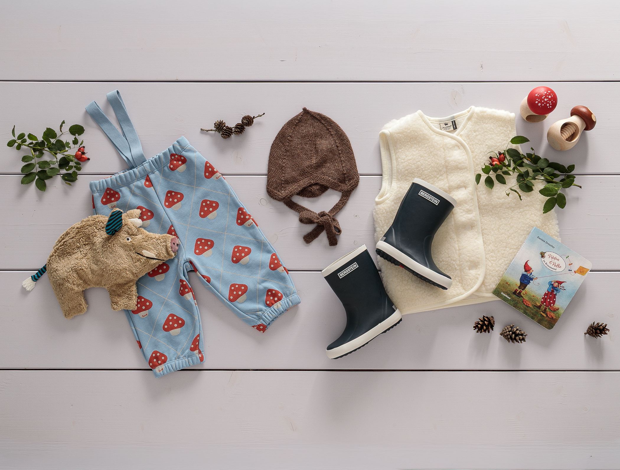 Diverse aktuelle Kinderkleidung und Babykleidung aus Baumwolle Wolle Seide für Frühjahr und Sommer in pastelligen Farben und Blümchenmuster liegen auf einem Dielenboden