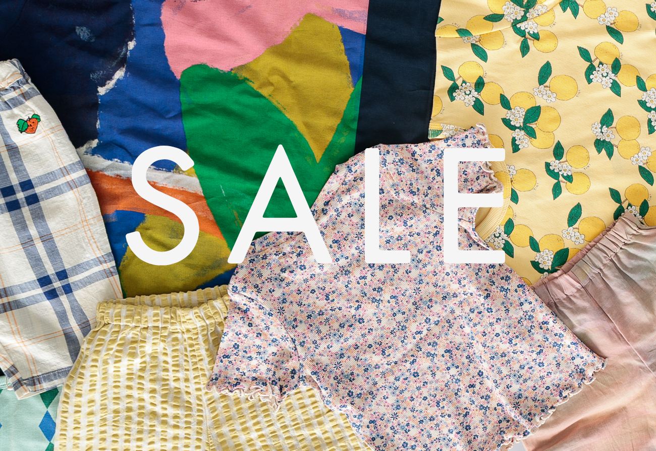Diverse aktuelle Kinderkleidung und Babykleidung aus Baumwolle Wolle Seide für Frühjahr und Sommer in pastelligen Farben und Blümchenmuster liegen auf einem Dielenboden