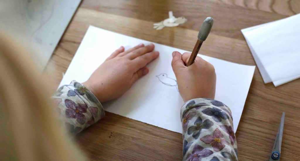 Ein Kind malt eine Taube auf Papier.