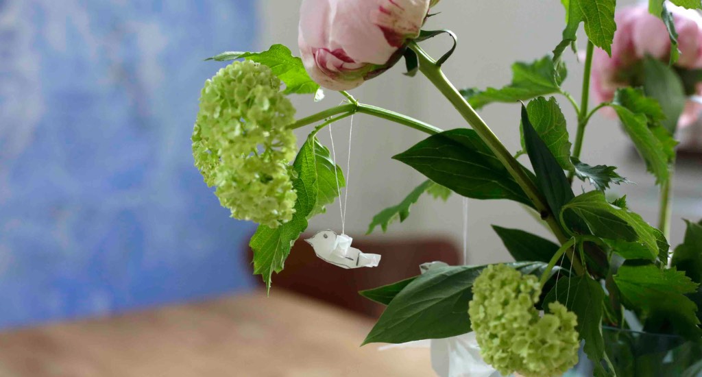 Die fertige Taube aus Papier hängt am Blumenstauß mit Pfingstrosen.